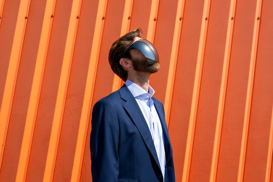 Businessman in suit using VR headset outdoors with orange background