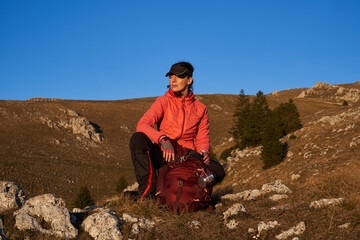 A female hiker unpacks her gear and relaxes after a challenging day of mountain trekking, enjoying the tranquility of a sunset