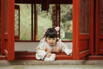 Young girl in traditional outfit by a red window.