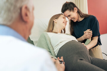 Intimate moment between a lesbian couple during a pregnancy exam, touching foreheads with love and...