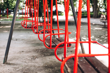 Empty red swings on playground in summer park, close-up perspective.