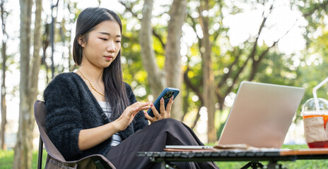 Portrait of young girl using laptop and a phone while sitting in the park