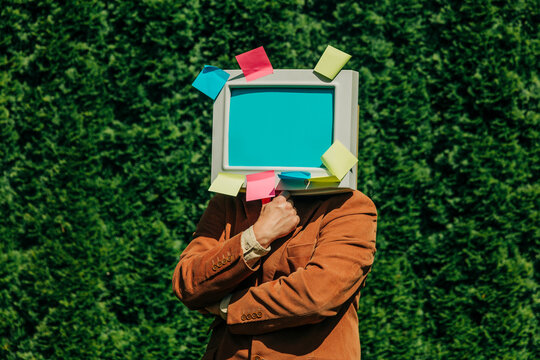 Person with retro computer monitor head with sticky notes in outdoor setting
