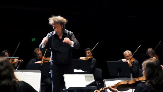 A passionate orchestra conductor dynamically leads musicians during a grand classical music performance on a darkened stage.