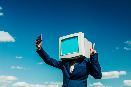 Businesswoman with retro monitor head making selfie under blue sky