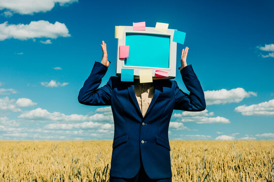 Businesswoman with retro monitor head and sticky notes in wheat field