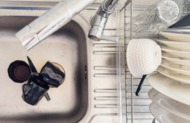 Dirty black mugs in stainless steel kitchen sink, showing everyday home cleaning tasks, mess and...