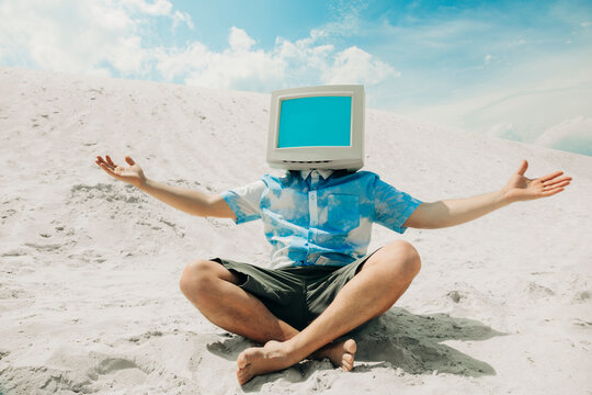 Person with CRT monitor head relaxing on sand dune in summer