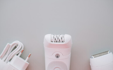 A modern white epilator stands upright against a two-tone background of light grey. 