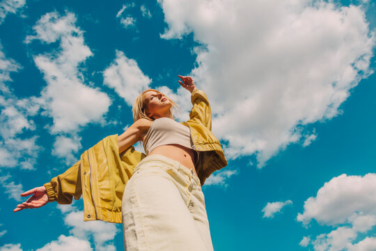 Stylish woman with blonde hair posing outdoors against blue sky