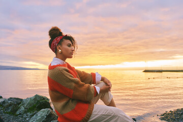 Outdoor portrait of young african woman admiring amazing sunset by the lake