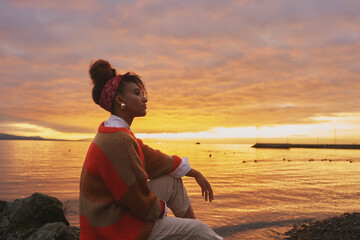 Outdoor portrait of young african woman admiring amazing sunset by the lake