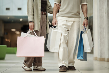 Caucasian woman and man walking together holding multiple shopping bags in modern furniture store,...