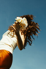 Young woman dancing with flowers under a clear blue sky, back view
