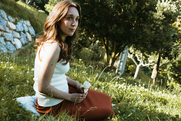 Young woman sitting peacefully in a garden holding a white rose