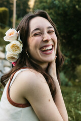 Portrait of joyful young woman laughing with roses in her hair in the garden