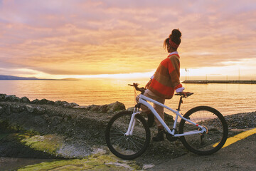 Outdoor portrait of happy african woman admiring sunset over the lake during bike ride
