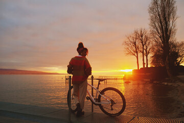 Outdoor portrait of happy african woman admiring sunset over the lake during bike ride