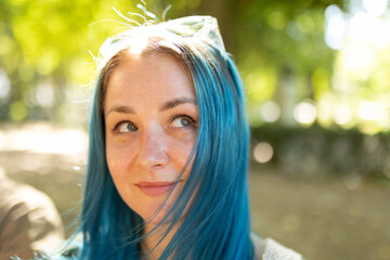 Young woman with blue hair looking away and smiling in a park
