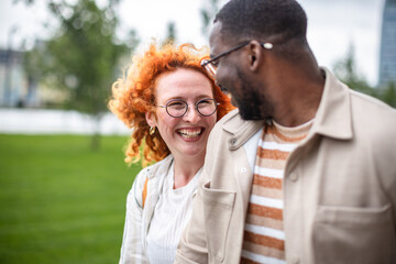 Black man and ginger woman enjoying a sunny day together in a park while sharing smiles and laughter