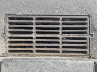 Rectangular metal storm drain grate embedded in asphalt pavement.