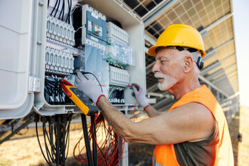 Side view of an electrician measuring electricity with voltmeter at solar power plant.