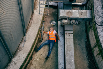 An injured old heavy industry worker lying down on a ground in pain.