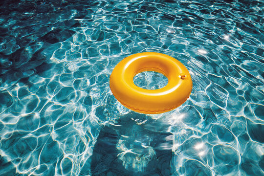 A bright yellow inflatable swim ring floats on clear, rippling blue water.
