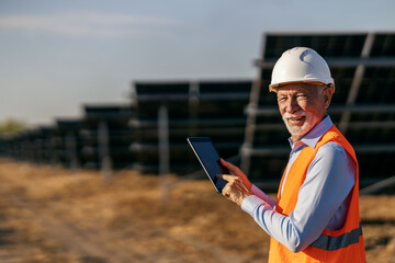 Portrait of an old engineer scrolling on tablet at solar plant while looking at camera.