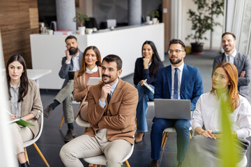 Group of businesspeople sitting in audience and listening to presentation.