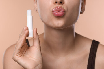 Young woman with lip balm on beige background, closeup