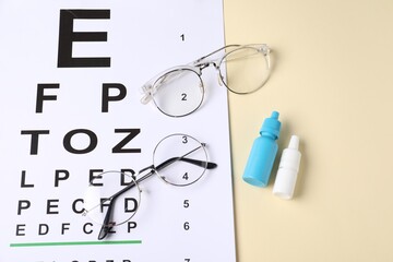 Vision test chart, glasses and bottles of medical drops on beige background, above view