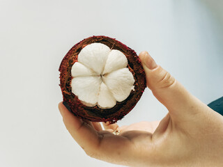Interior of fresh mangosteen fruit showing white segmented flesh inside thick purple rind,...
