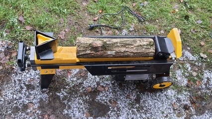 Log splitter machine splitting wood logs on snowy ground