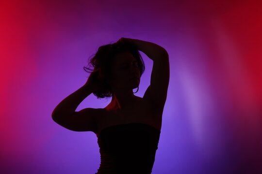 Silhouette of woman posing in neon lights on color background - Powered by Adobe