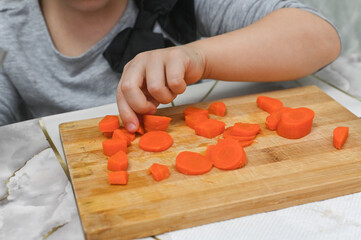 Child's small hands master knife techniques with soft carrots under adult supervision. Perfect image for parenting blogs about teaching kids kitchen safety.
