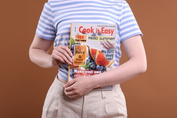 Woman with lifestyle magazine on brown background, closeup