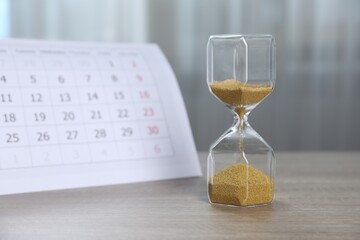 Deadline. Hourglass with flowing sand and calendar on wooden table indoors