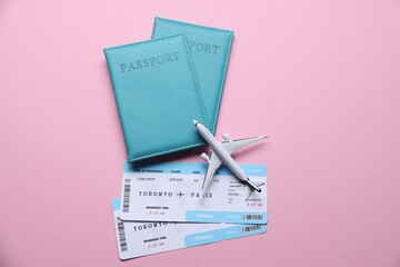 Airplane model, flight tickets and passports on pink background, flat lay