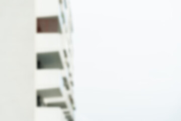 Out-of-focus blurred white modern apartment building with balconies against a bright sky. Suitable...