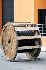 Large wooden spool with black industrial cable near modern building on concrete surface
