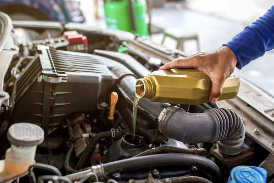 Car mechanic replacing and pouring fresh oil into engine at maintenance repair service station