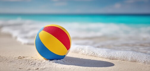 Obraz premium The colorful volleyball rests on the sandy beach near the turquoise ocean.