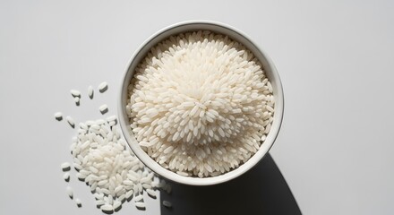 Top View of White Rice in Bowl with Scattered Grains on White Surface.