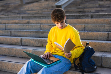 College student studying outdoors using laptop and textbook on stairs