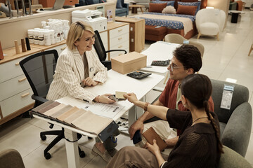 Caucasian young adult woman sitting at desk assisting Caucasian young adult man and woman choosing...