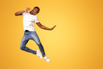 Funny black guy in casual outfit bouncing over orange studio background, full length shot. Playful...