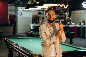 Standing and posing. Handsome man with a pool table game