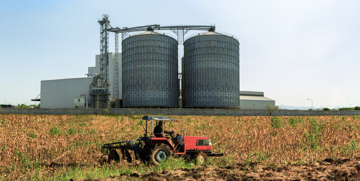Agricultural Silos - Building Exterior, Storage and drying of grains, wheat, corn, soy, sunflower against the blue sky  with farm tractors in the foreground.