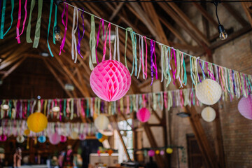 Bright paper lanterns and hanging ribbons decorating the wooden beams of a rustic barn venue for a festive indoor celebration. Suitable for commercial use. © Raivo